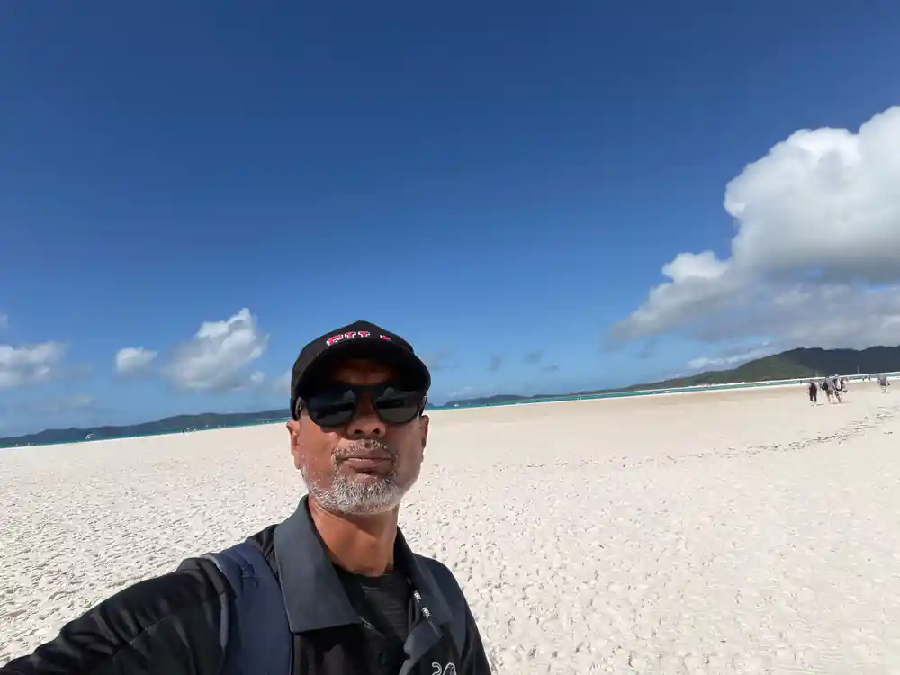 Man on white sand beach with island and lagoon background