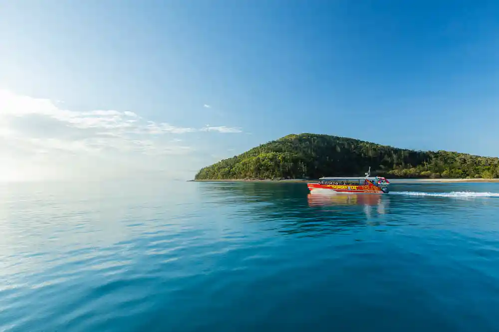 Orange boat in calm blue water near forested island