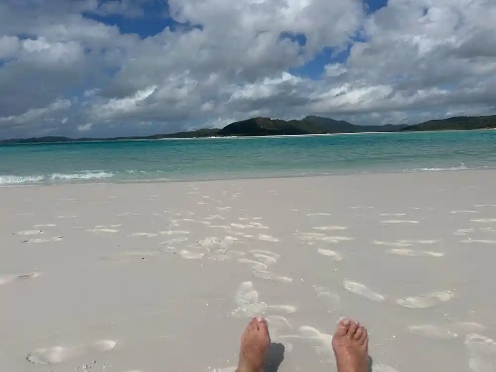 Person's feet on white sand beach with turquoise water