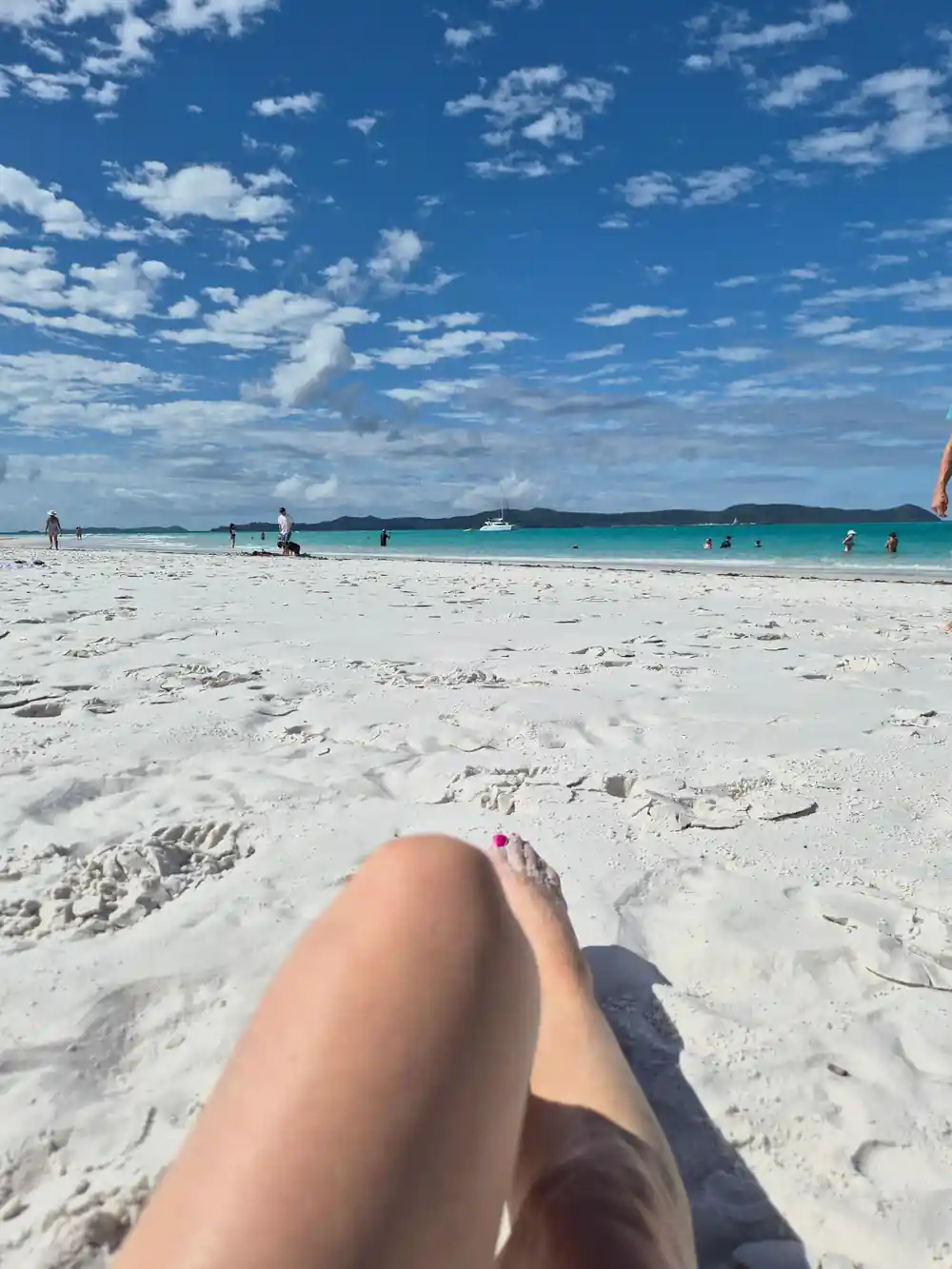 Person's legs on white sand beach facing turquoise water