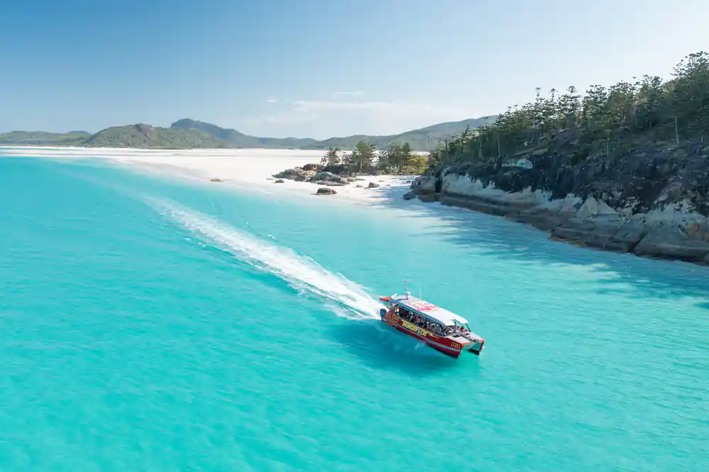 Red speedboat traveling along white sand coastline