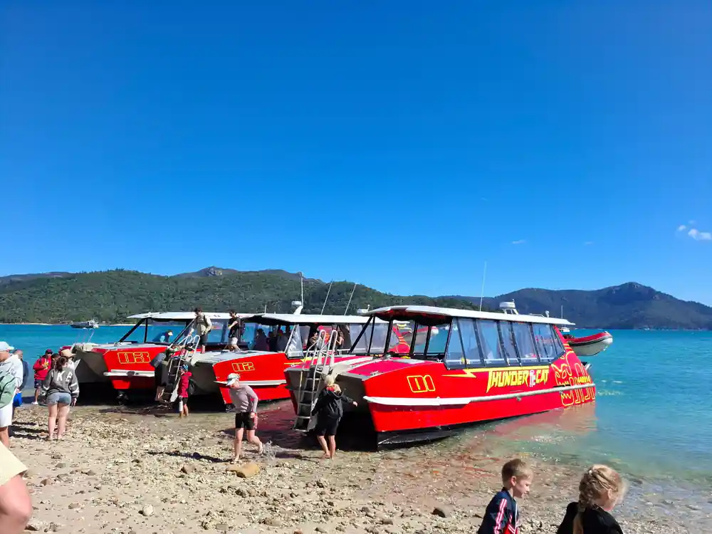 Red tourist boat beached on sand with passengers boarding