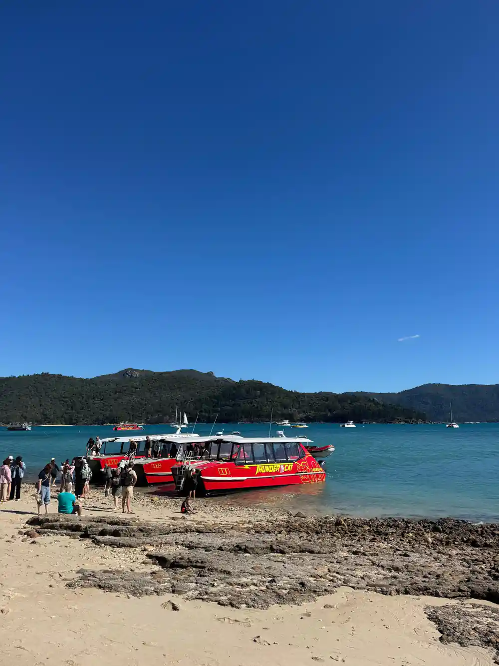 Red and white boat moored at sandy beach with people