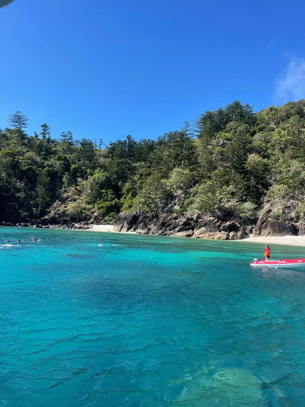 Swimmers and red boat in clear turquoise bay