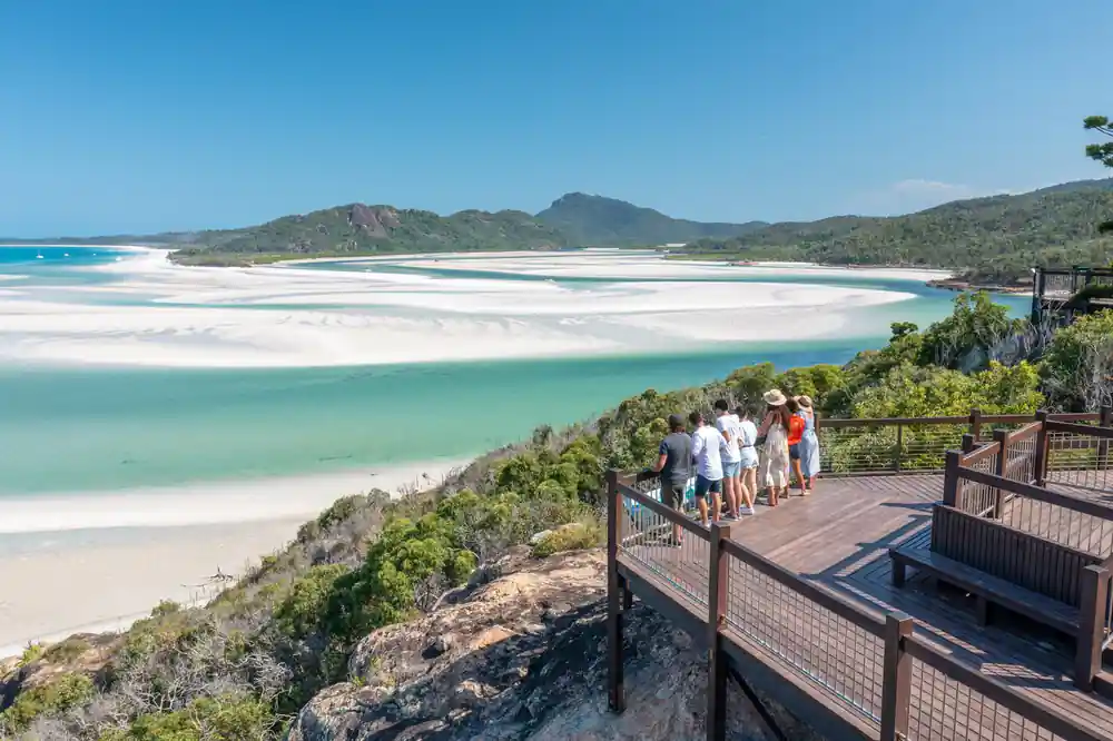 Tourists viewing white sand beach from elevated viewpoint