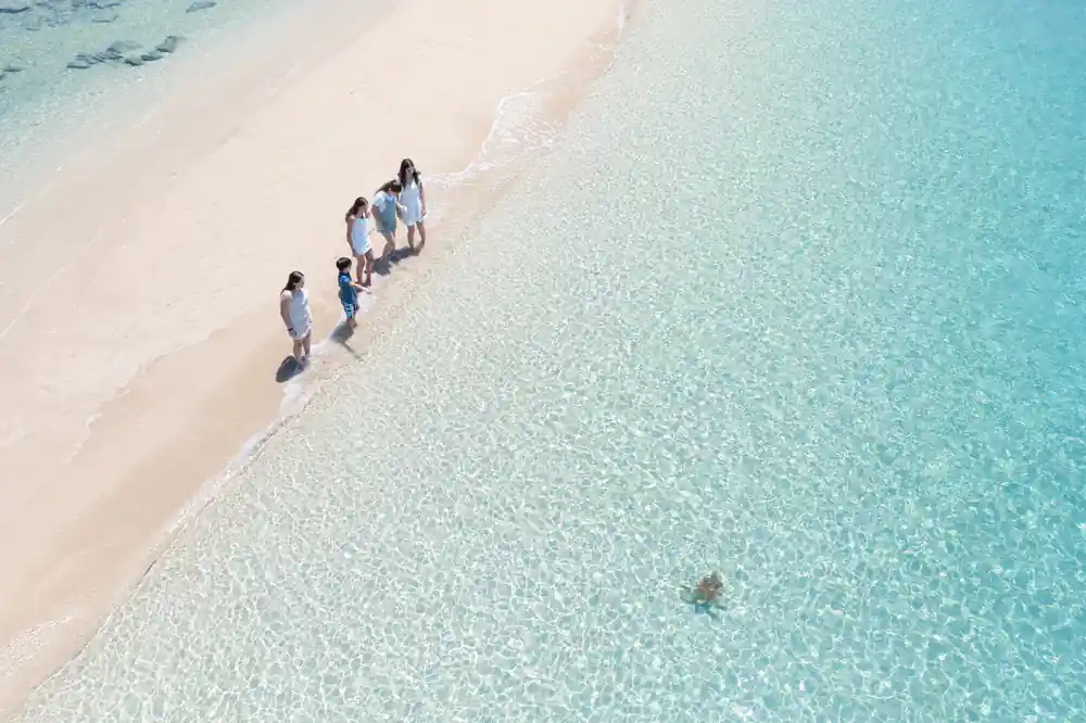 Tourists walking along white sand beach shoreline