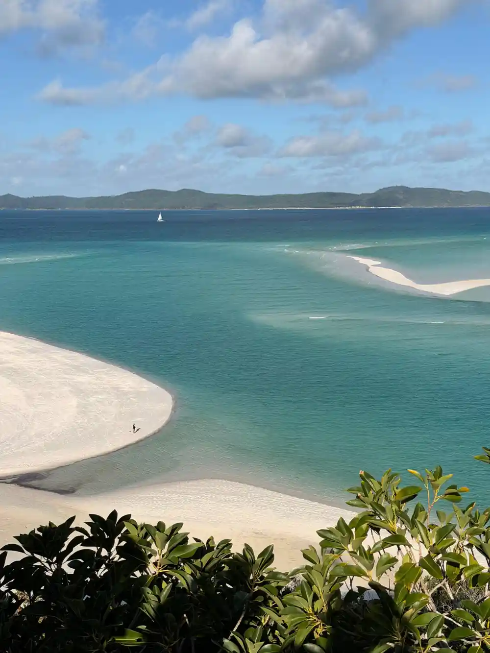 Turquoise lagoon with white sand beach and sailboat anchored offshore