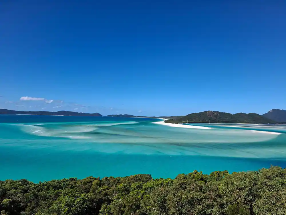Turquoise shallow bay with white sand and forested headlands