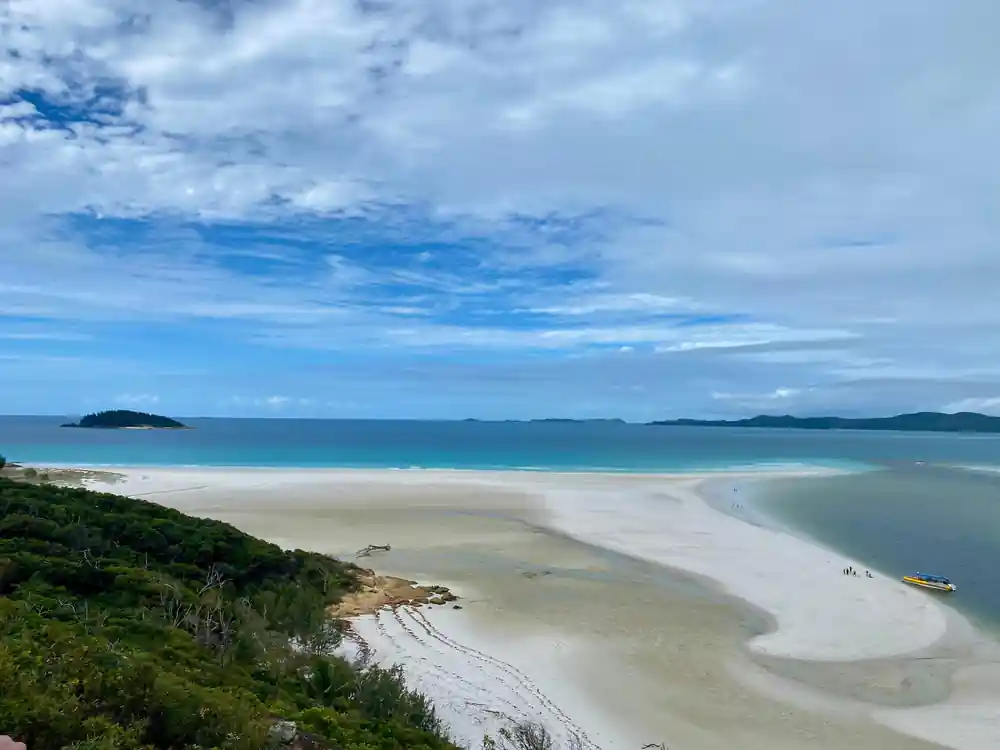 White sand spit in turquoise bay with forested hills