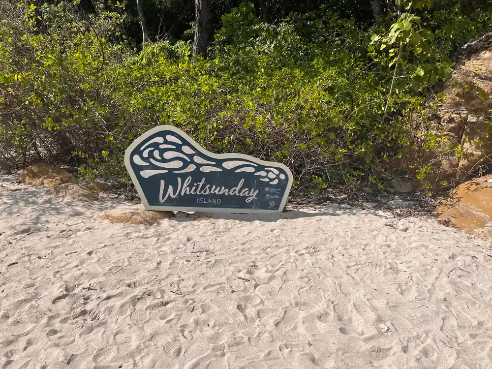 Whitsunday sign on sandy beach with vegetation background