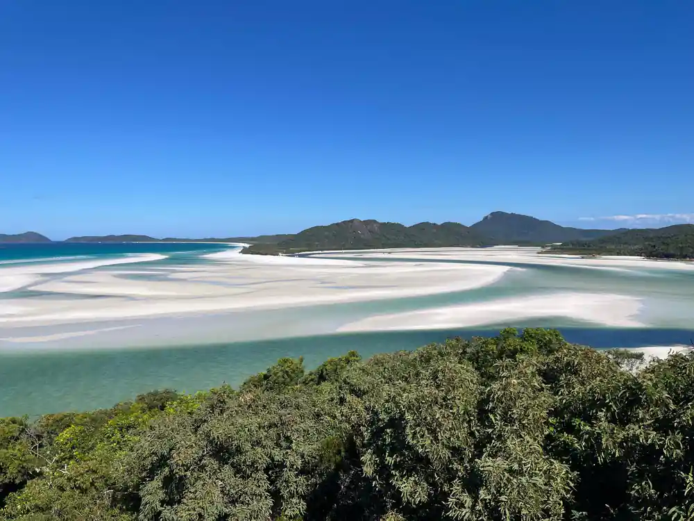 Wide turquoise bay with white sandy spit and green forested hills